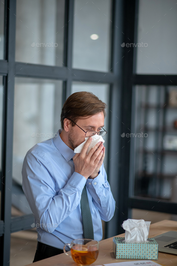 Businessman drinking tea and using napkins while sneezing