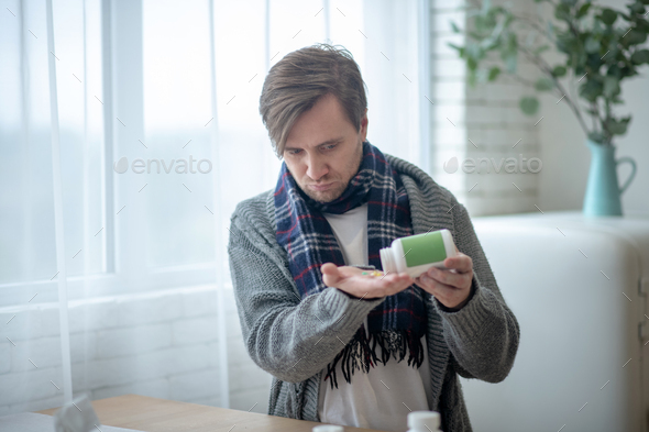Dark-haired man wearing checked scarf taking vitamins
