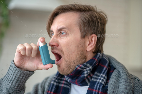 Blue-eyed man being out of breath applying inhalator