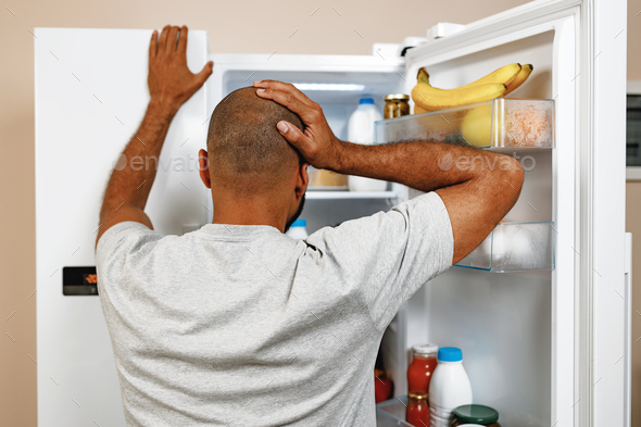 African american man standing in front of open fridge and choosing food