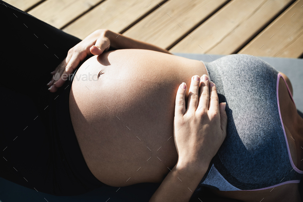 Young pregnant woman doing yoga outdoor - Focus on right hand holding belly
