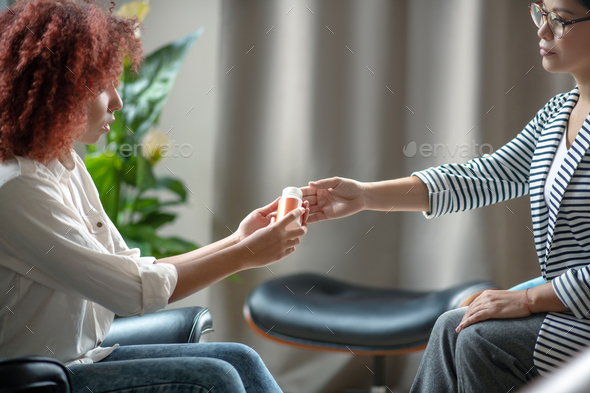 Curly red-haired woman taking sleeping pills from psychologist