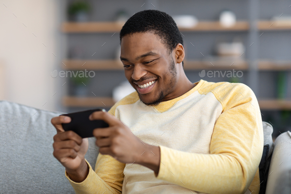 Happy black guy playing game on mobile phone