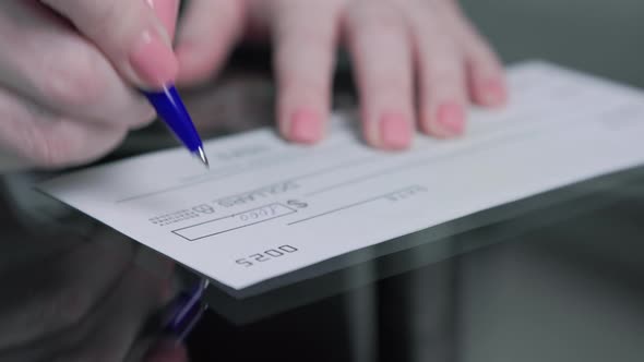 business woman hand signs and filling bank check for one thousand 1000 dollars alt