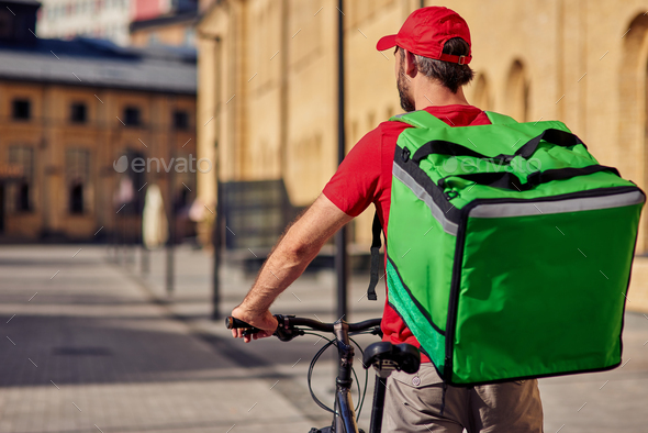 Male courier with refrigerator bag riding bicycle