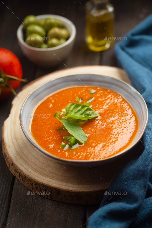 traditional spanish dish gazpacho with green leaves on a dark wooden table