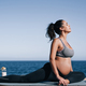 Pregnant woman doing yoga exercise routine next to the beach