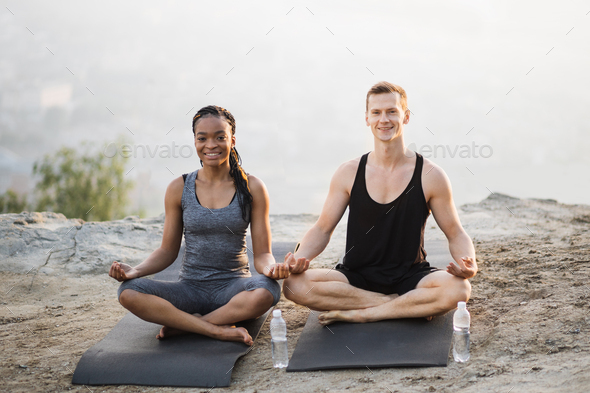 Multicultural couple meditation on yoga mat outdoors