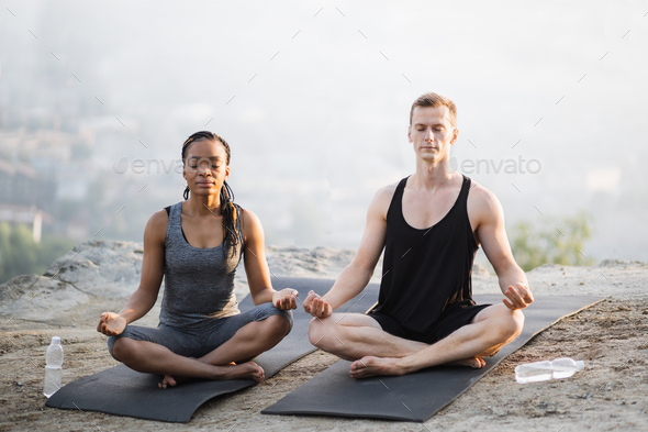 Multicultural couple meditation on yoga mat outdoors