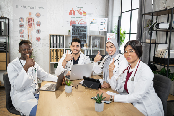 Multiracial doctors showing thumbs up at office meeting