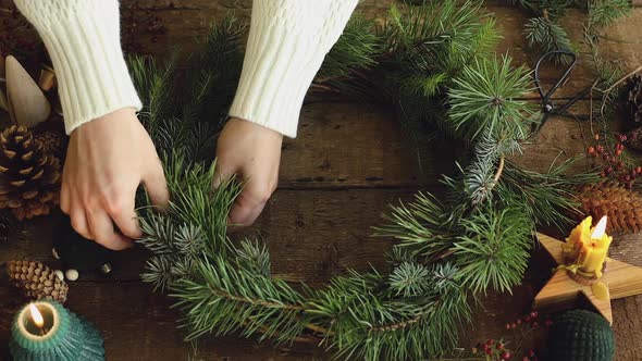 Making Christmas wreath on rustic wooden table with candle, decorations, cones