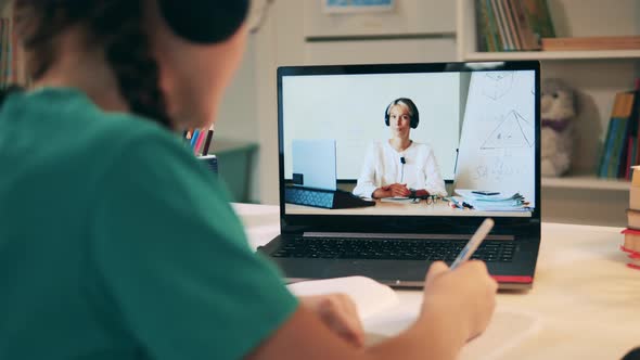 A Girl Is Taking Notes After a Lady Teacher While Studying Online alt