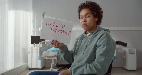 Young African Patient in Wheelchair at Hospital Ward Holding Health Insurance Poster alt
