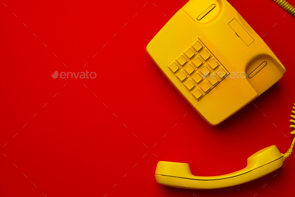 Yellow landline phone on red background top view