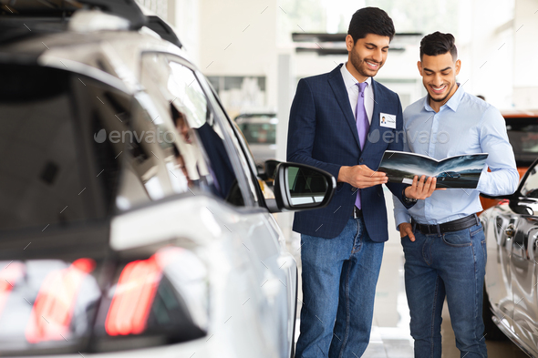 Middle-eastern guy having conversation with sales assistant in auto showroom