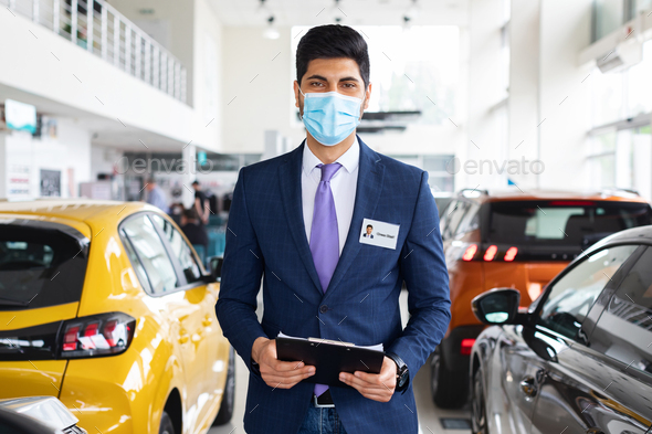 Salesman middle-eastern man in face mask posing in auto showroom