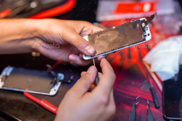 A man is repairing a mobile phone. In the frame, his hands and details of the device. repair shop