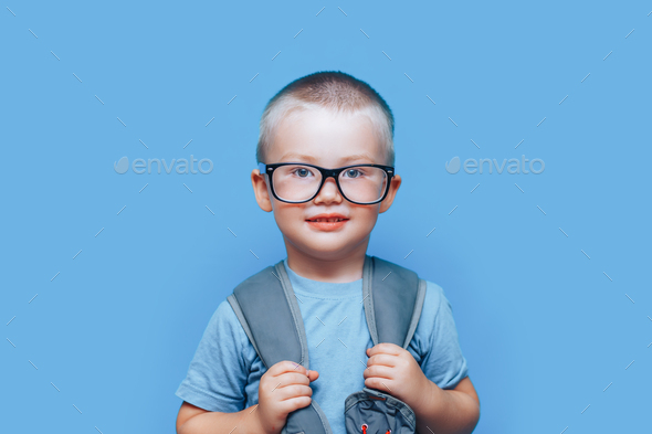 pretty blonde boy on blue background with backpack unhappy, sad, child don\'t want go to school