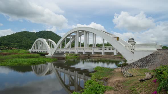 Time lapse of Tha Chomphu White Bridge, Lamphun, Thailand with lake or river, forest trees alt