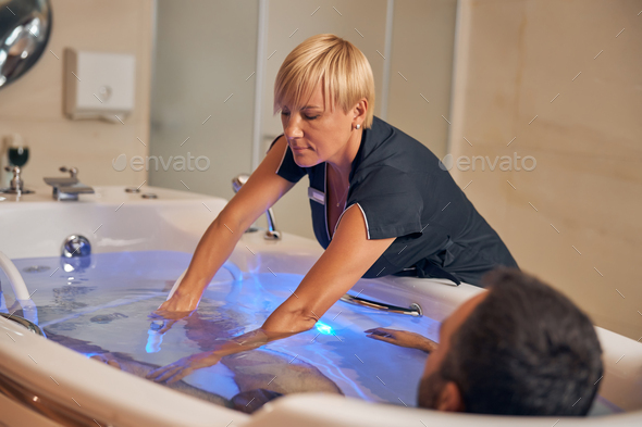 Female beautician performing hydromassage procedure in spa salon