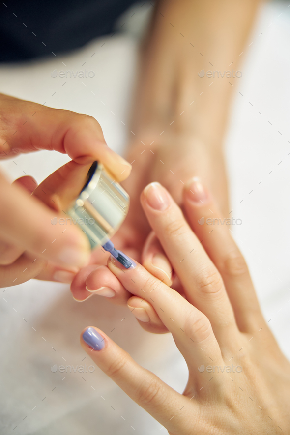 Beautician painting woman finger nails in blue Stock Photo by svitlanah