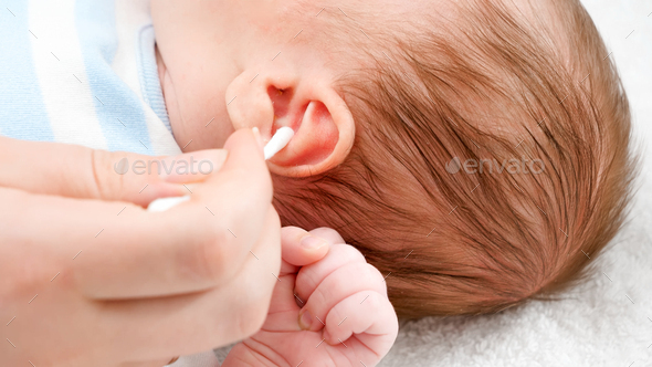 Closeup of mother using cotton swabs to clean little baby\'s ears from ear wax
