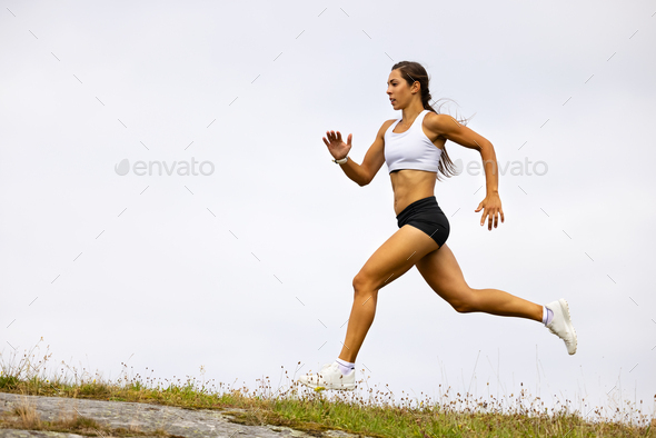 A strong athletic running female athlete on a - Stock