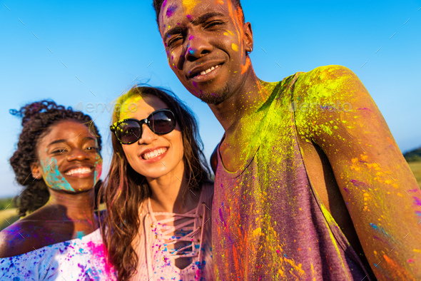 cheerful young multiethnic friends with colorful paint on clothes having fun together at holi
