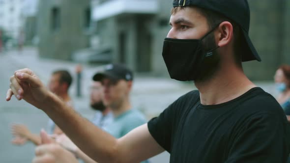 Rebel Regulations Activist in Face Mask Claps Hands in Crowded Marching People alt