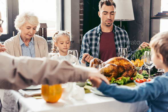 beautiful family holding hands and praying on thanksgiving before holiday dinner