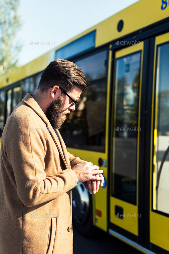 side view of bearded man checking time while standing on bus stop