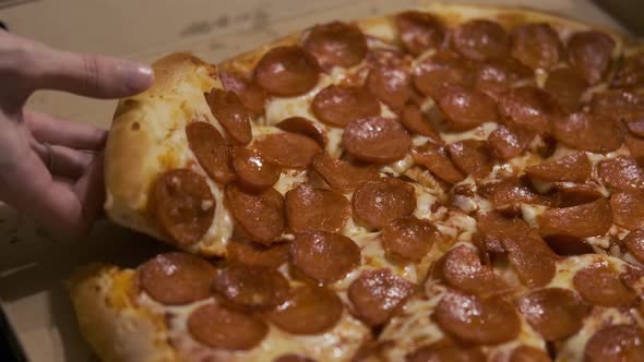 close-up of a woman's hand taking a slice of pizza with salami