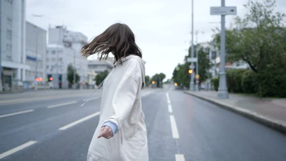 A Girl in a White Jacket Walks Early in the Morning on the Road in the City