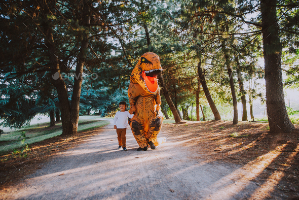Father and son playing at the park, with a dinosaur costume, having fun with the family outdoor