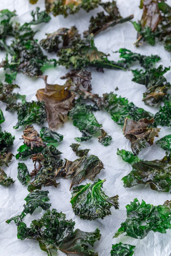 Three ingredient baked green kale chips with sea salt and olive oil, on a parchment, vertical