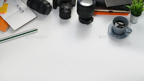 Working desk with camera, lens, potted plant, ruler, coffee cup and stack of notebook.