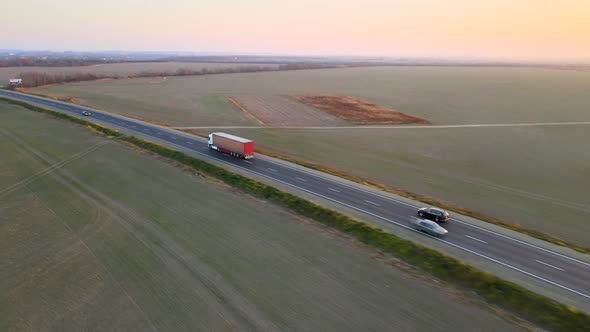 Aerial View of Semitruck with Cargo Trailer Driving on Highway Hauling Goods in Evening alt