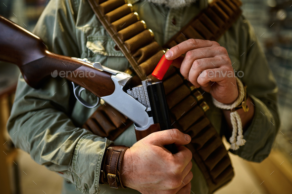 Male hunter with bandolier loads rifle, gun store - Stock Photo - Images
