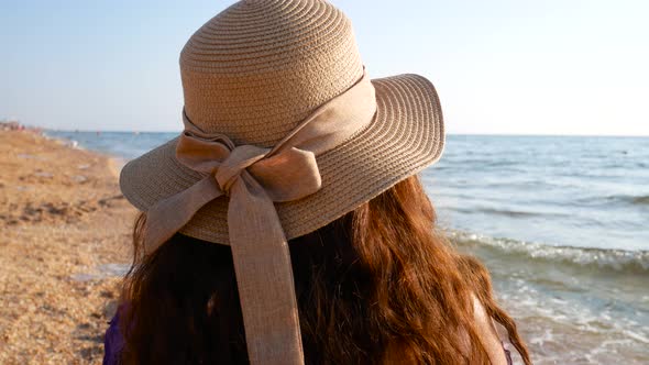 Girl in a Straw Hat with Brown Long Hair Looks at the Sea