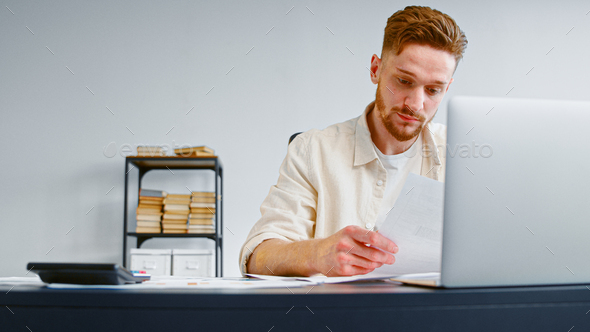 Concentrated financial director with beard looks through papers with business project at table