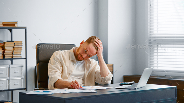 Young male financial director reads bank reports sitting at grey table