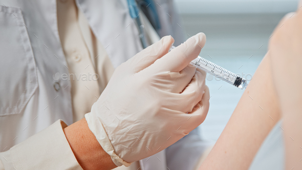 Professional general practitioner in white coat and sterile gloves injects hospital patient in arm - Stock Photo - Images