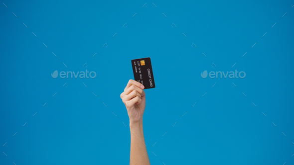 Young woman hand shows credit card for shopping online over blue background in studio.