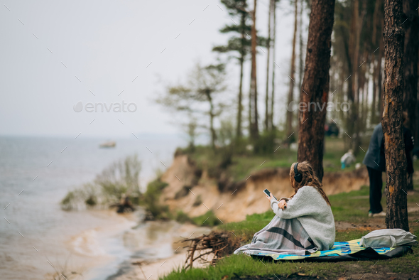 A young woman sits on the shore of a small lake near the forest - Stock Photo - Images