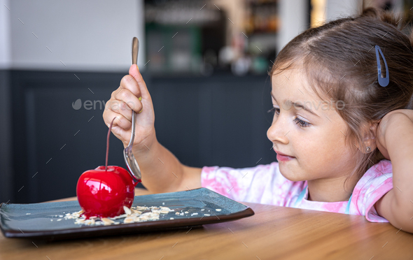 A little girl eats a cherry-shaped chocolate mousse, an unusual cherry cake.