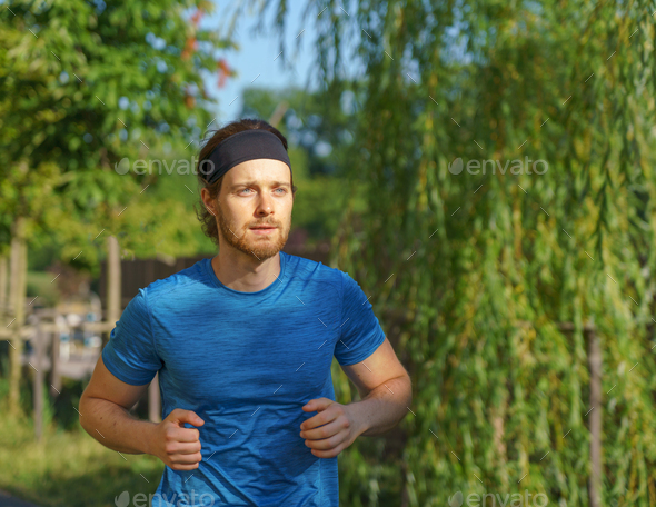 Athletic european man in sportswear jogging on road in green park on beautiful summer day - Stock Photo - Images