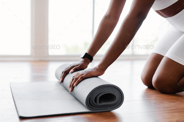 Young black woman unrolling yoga mat on floor - Stock Photo - Images