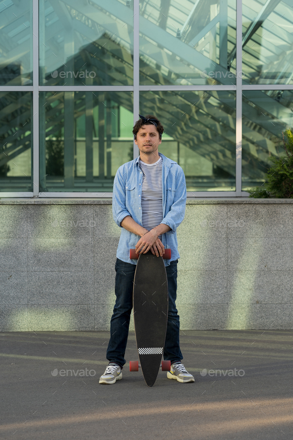 vedhæng gnier passager Stylish man holding longboard over city building. Hipster guy skateboarder  with skateboard outdoors Stock Photo by varyapigu