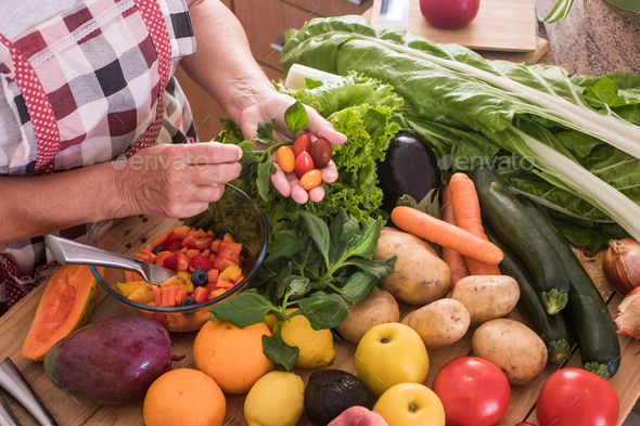 Hands of a woman cut fruit and select the best small tomatoes, wooden table with fruit and vegetable - Stock Photo - Images