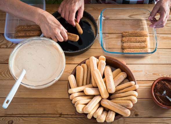 Two people in the kitchen preparing a sweet cake, the tiramisu. All ingredients on the wooden table - Stock Photo - Images